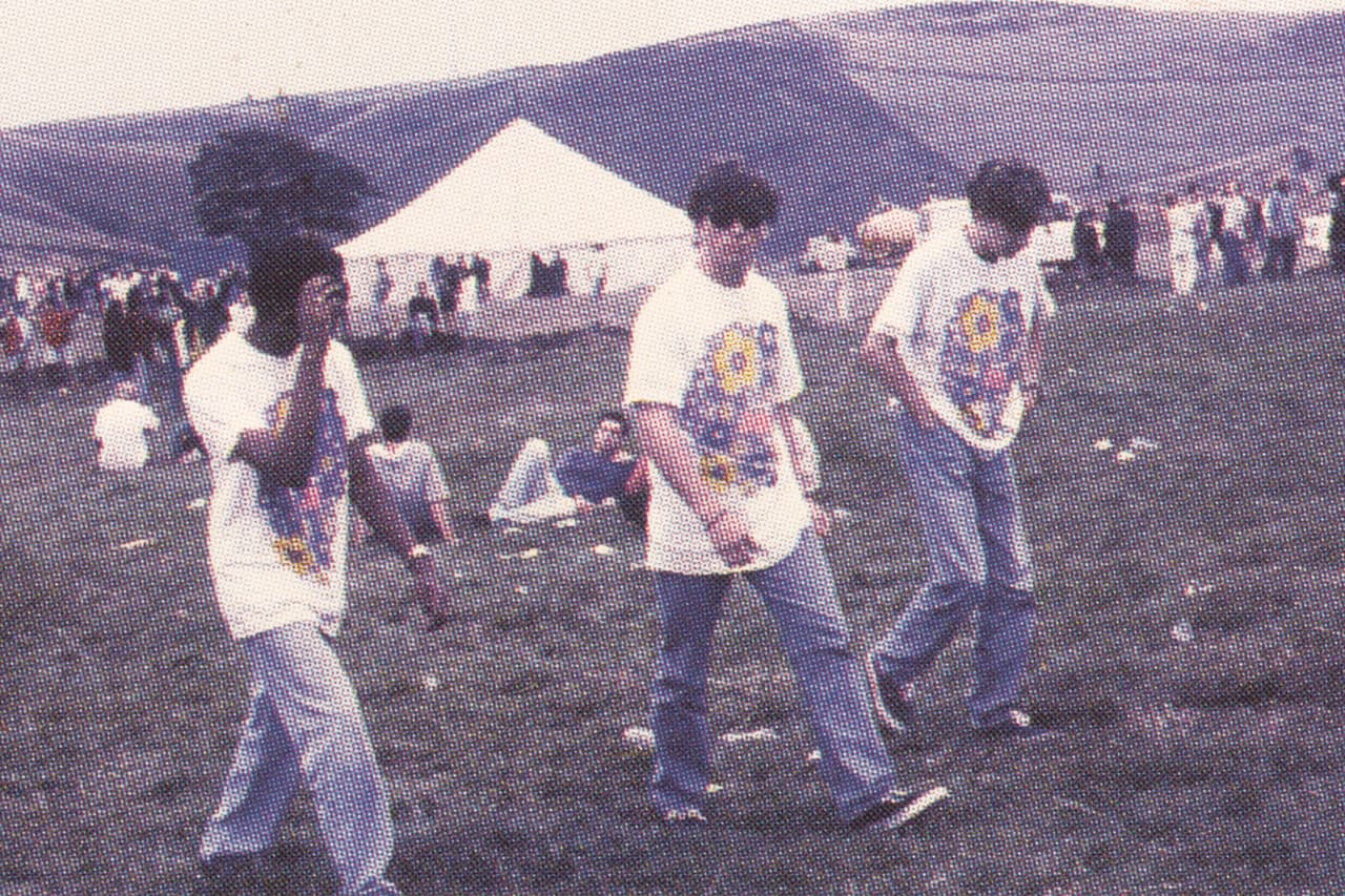 Festival-goers in printed T-shirts on a hillside, a marquee behind
